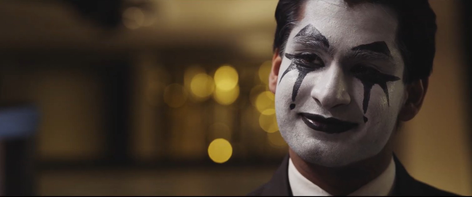 Still from Fools Rush In: a man in mime makeup smiles in close-up against warm out-of-focus lights