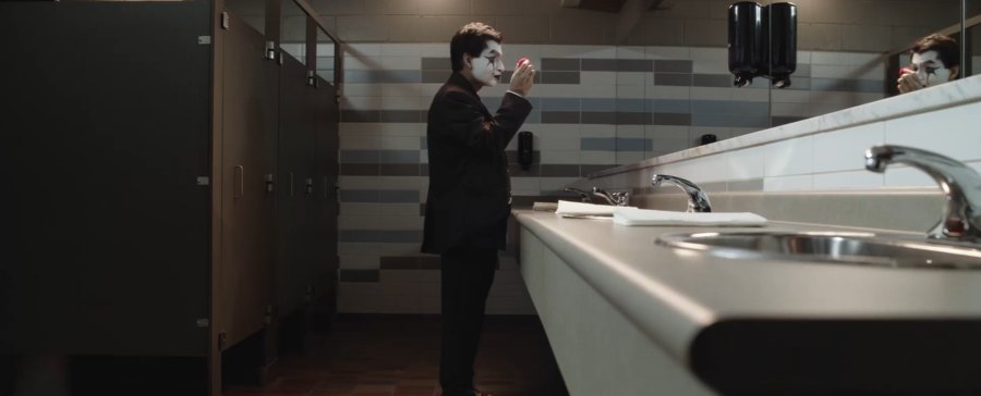 Still from Fools Rush In: a man in mime makeup checks a red clown nose in an office bathroom mirror