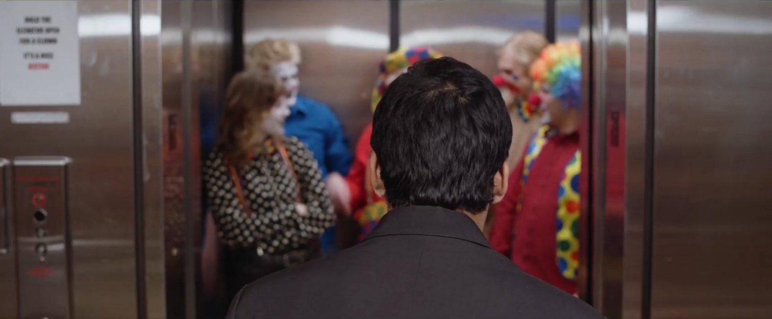 Still from Fools Rush In: seen from behind, a man faces an elevator crowded with clowns