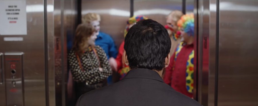 Still from Fools Rush In: seen from behind, a man faces an elevator crowded with clowns