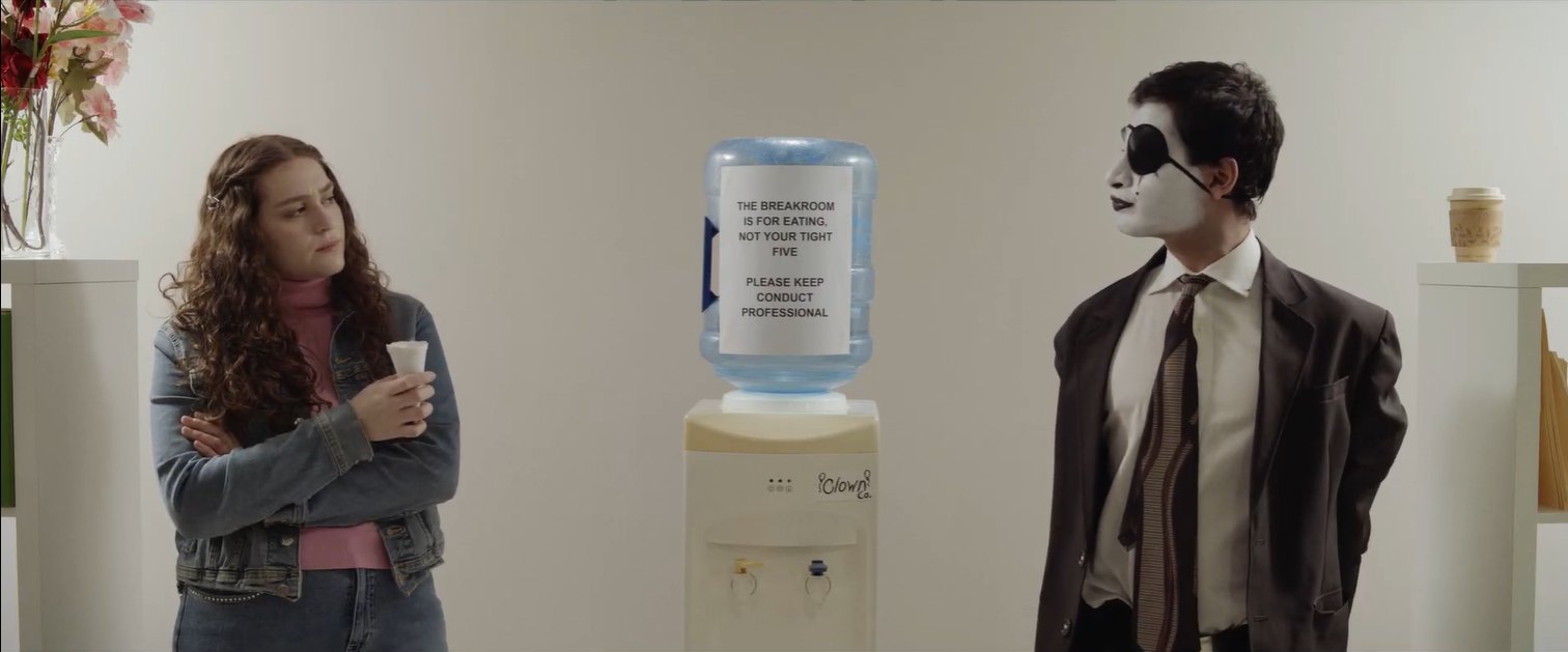 Still from Fools Rush In: a woman and a man in mime makeup stand on either side of an office water cooler
