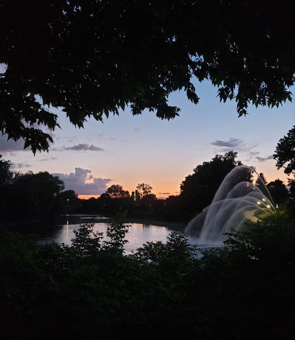 Fountain silhouetted against a sunset, framed by leaves