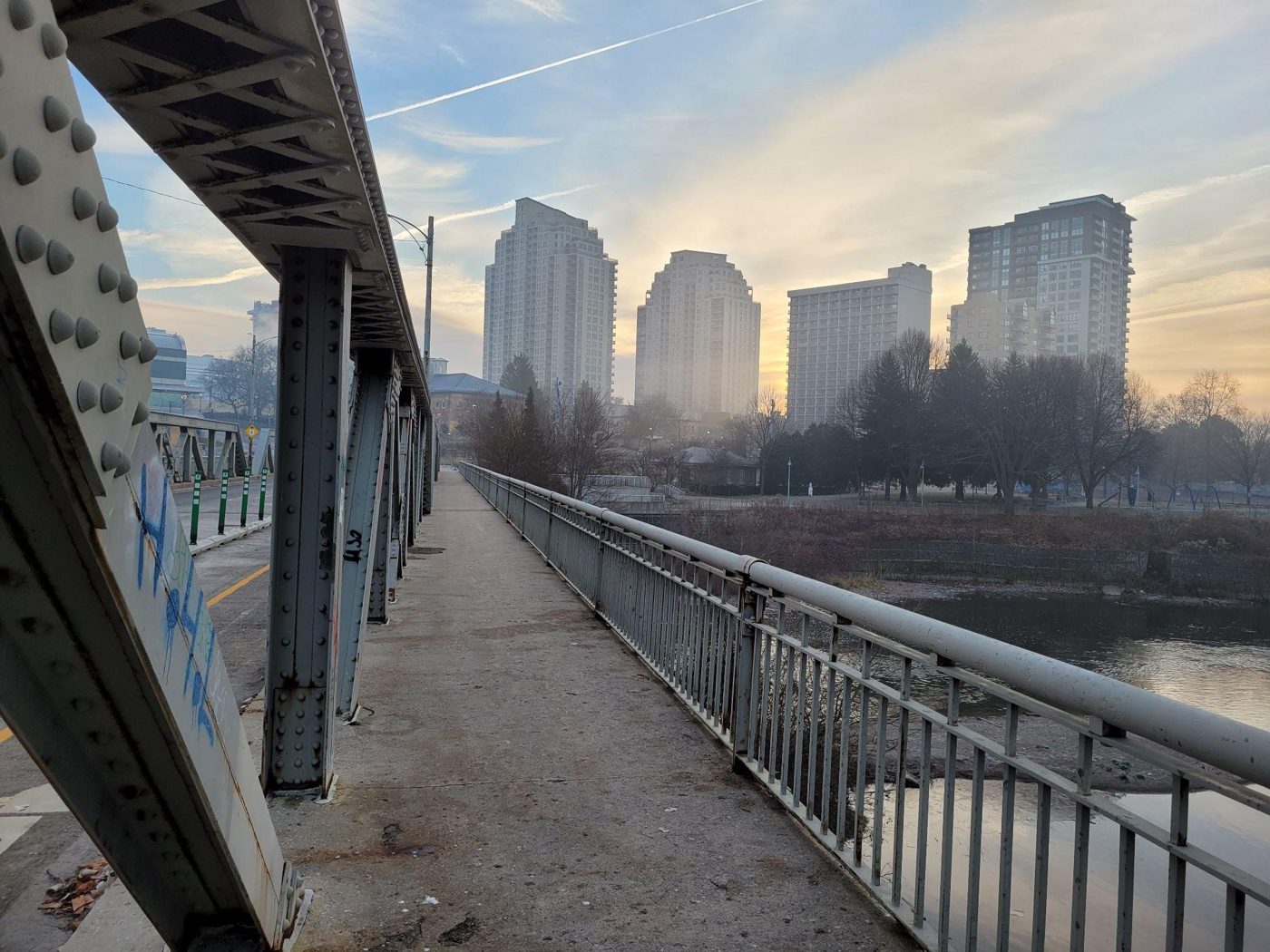 Steel footbridge leading toward a row of condo towers at dusk